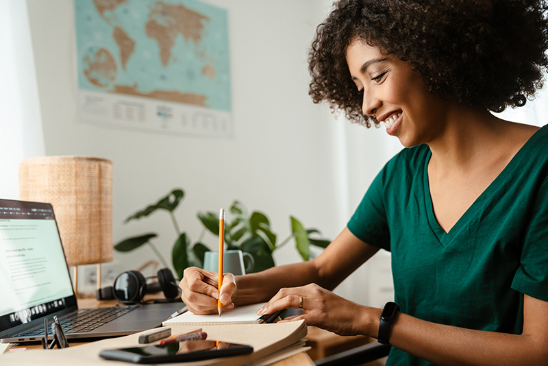 African american young woman using laptop and taking notes while sitting at desk
